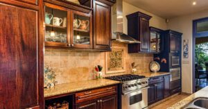 Image of dim-lit kitchen featuring dark hardwood cabinets and neutral tile backsplash